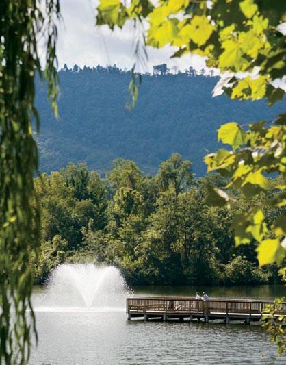 two people sitting on a bench in front of a lake with a fountain