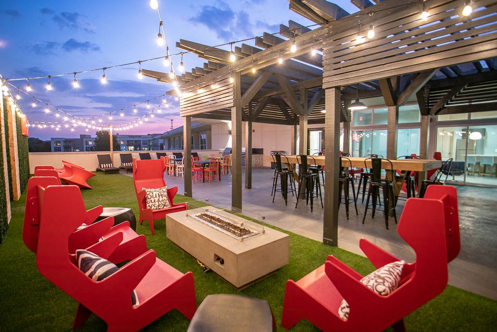 a patio with red chairs and tables and a fire pit