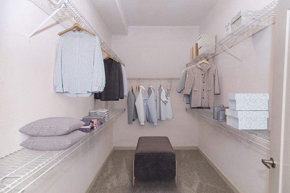 a walk in closet with clothes hanging on a rack and a black ottoman