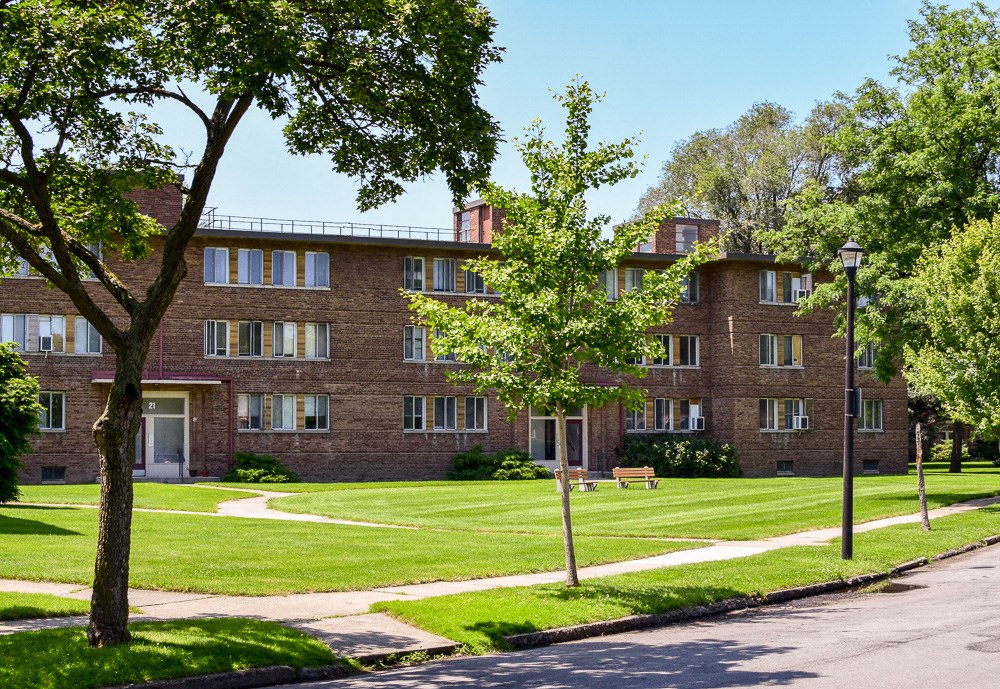 a brick building with a lawn and trees in front of it