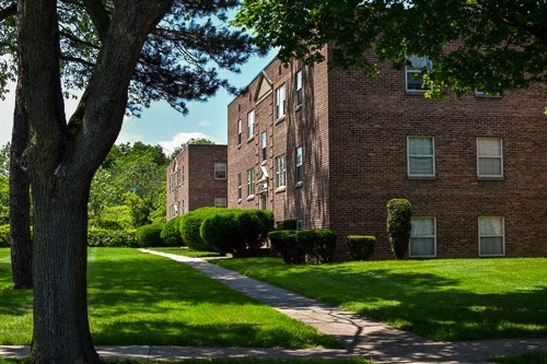a brick building with green grass and trees and a sidewalk