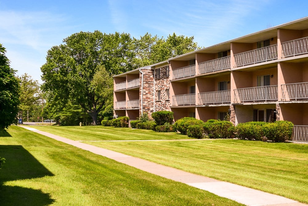 an exterior view of an apartment building with a lawn and trees