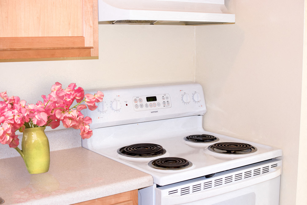 a kitchen with a stove and a vase with pink flowers