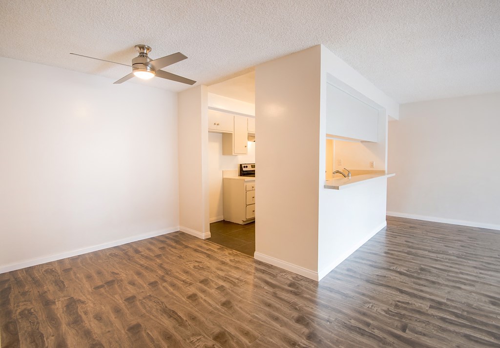 an empty living room with a ceiling fan and a kitchen