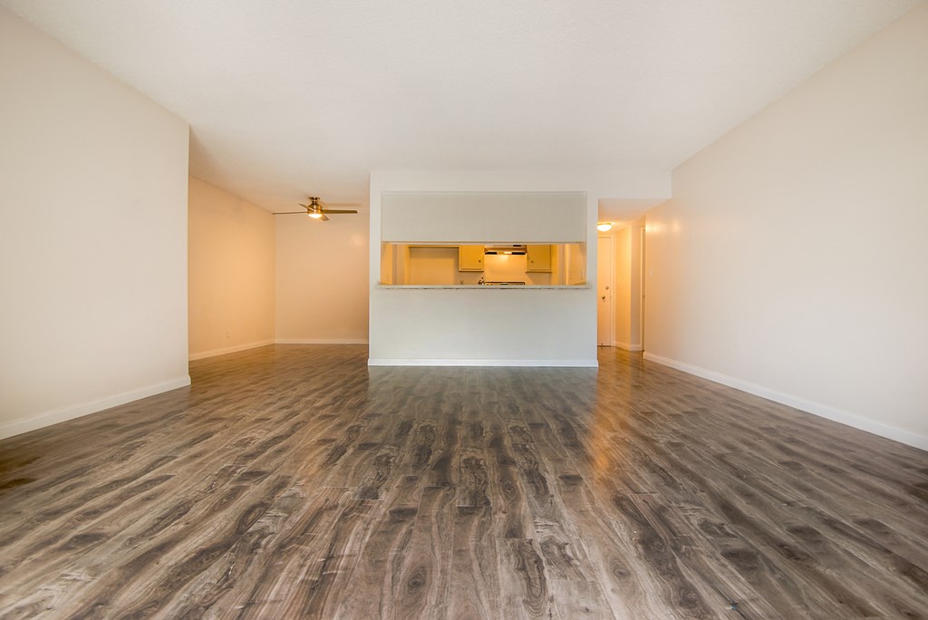 an empty living room with wood flooring and a kitchen