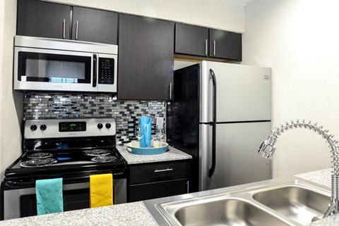 A kitchen with a black and white color scheme featuring a stove, microwave, refrigerator, and a sink.
