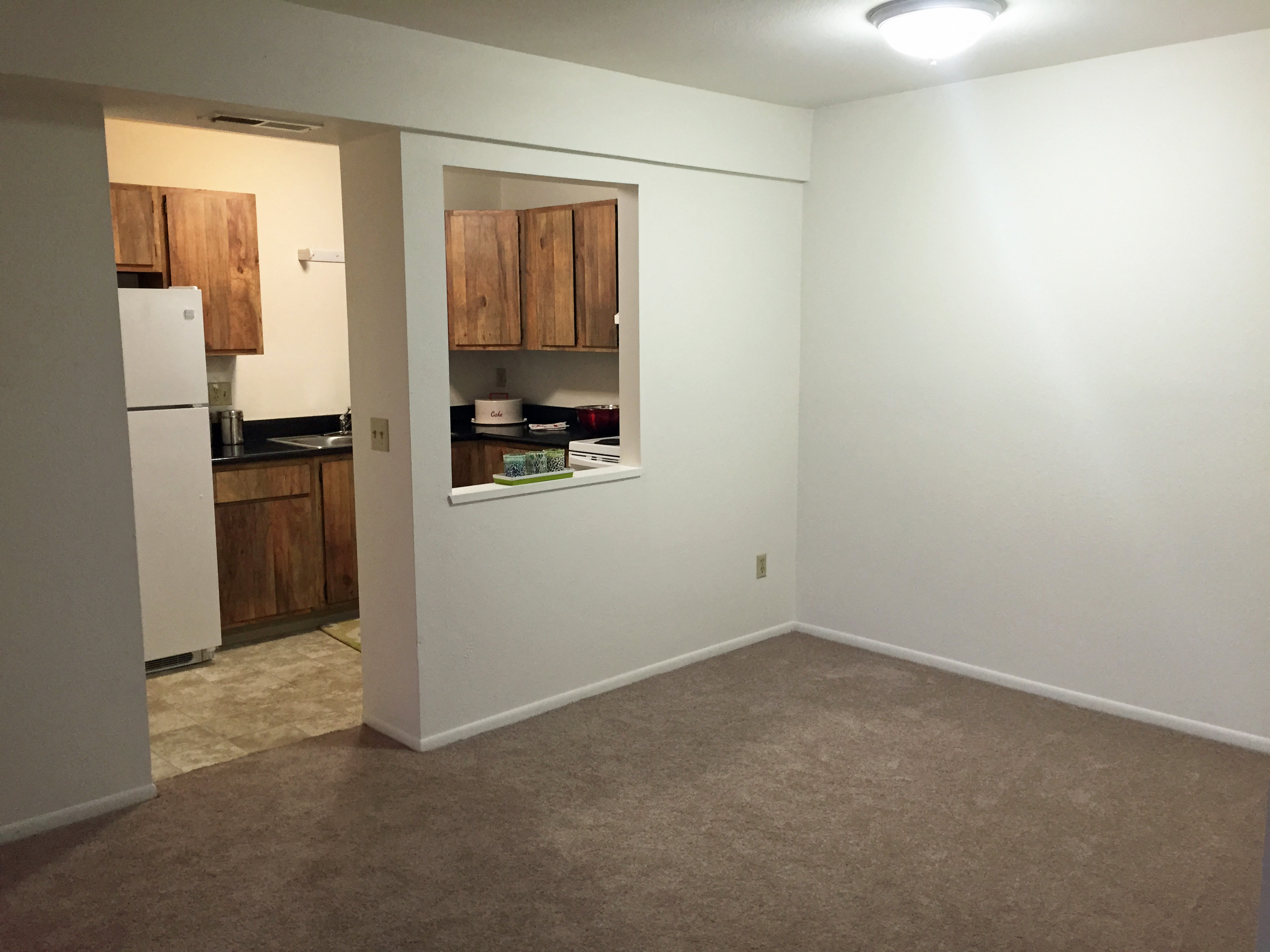 an empty living room with a window and a kitchen