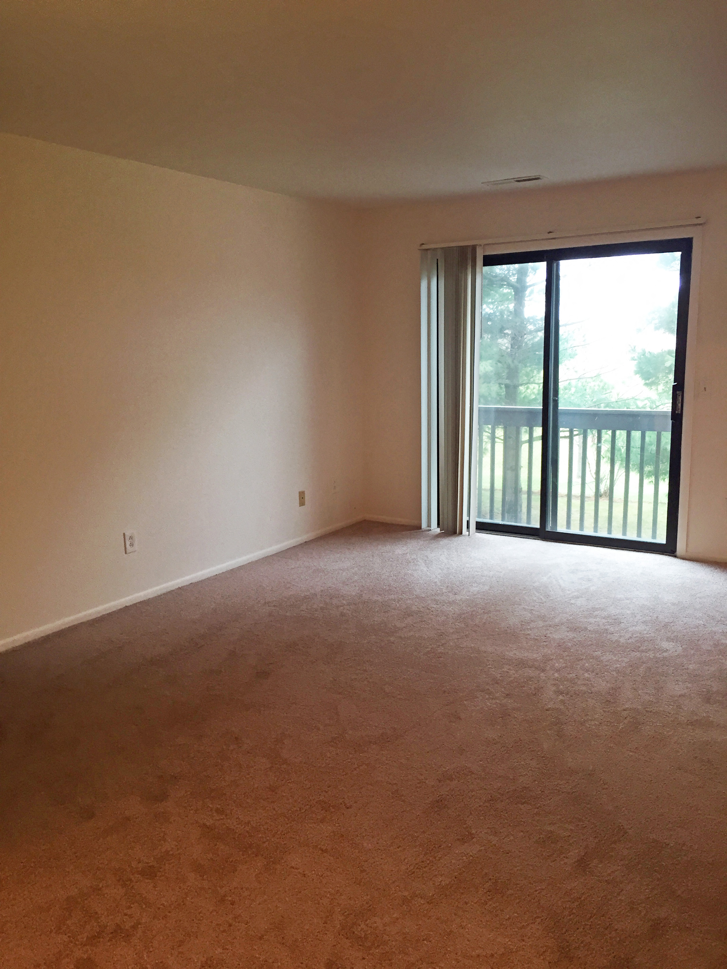 an empty living room with a sliding glass door to a balcony