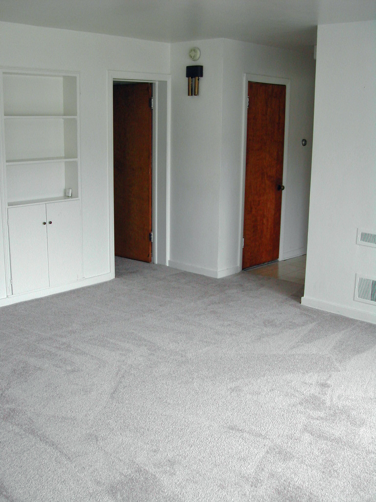 an empty living room with a carpeted floor and two doors