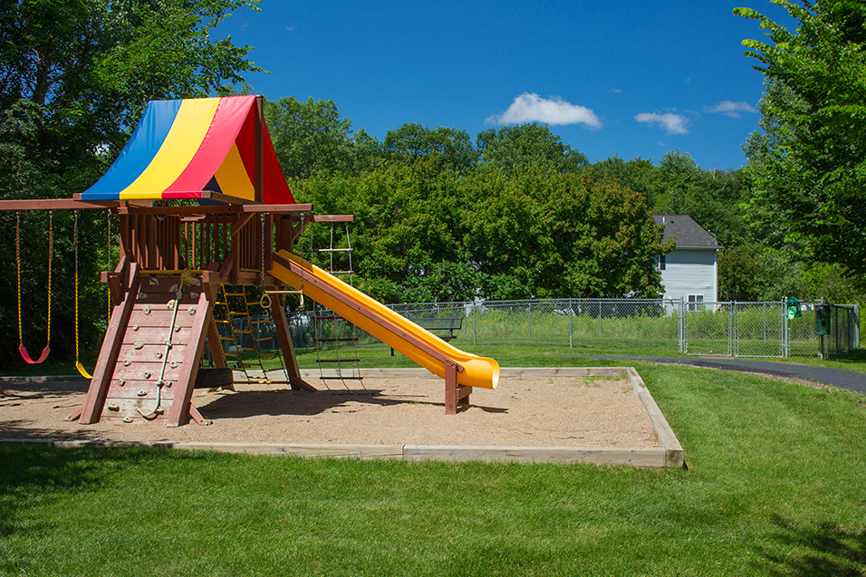 children's outdoor playground with swings, climbing wall, slide, and rainbow canopy, on a sunny day