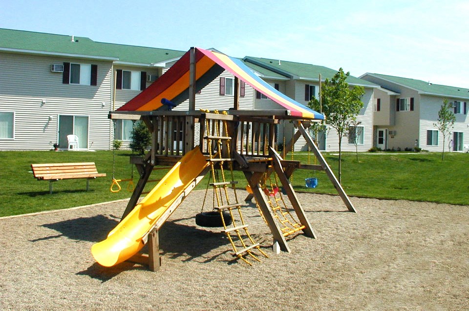 a playground with a swing set and slide in front of a house