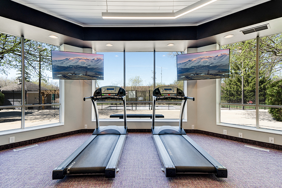 Fitness room with treadmills facing TVs and large windows