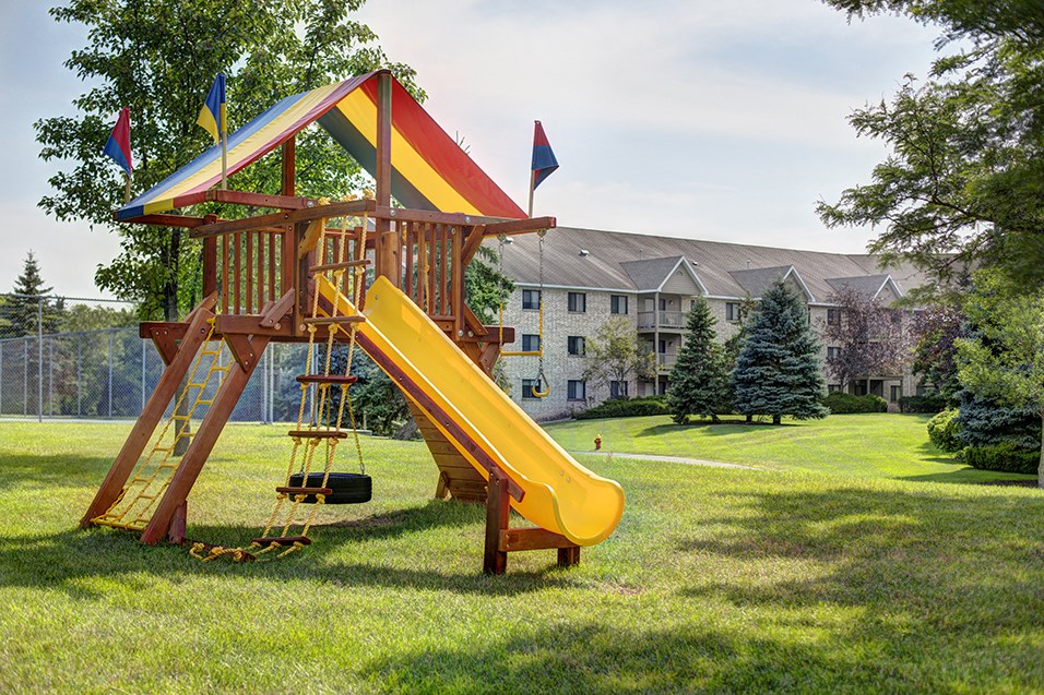 a swing set with a yellow slide in the middle of a yard
