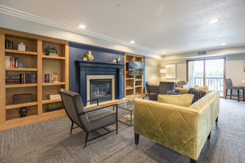 Community room with a variety of seating in front of a fireplace, pillared by bookshelves