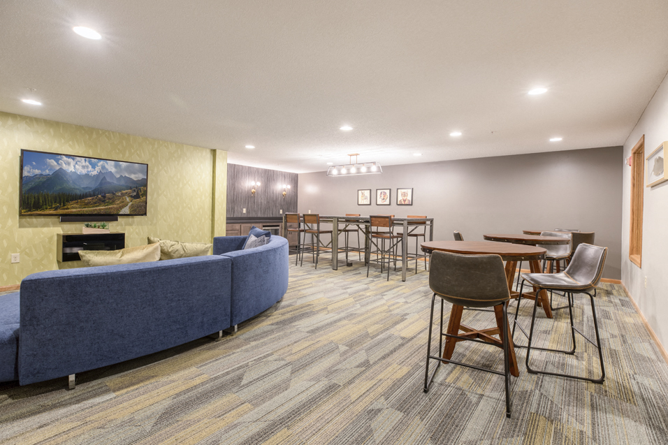 Lounge with tables and chairs, and a blue circular couch facing a wall-mounted TV