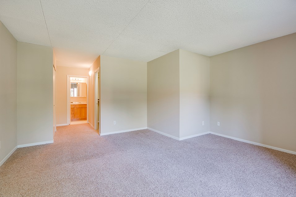 an empty living room with carpet and a hallway to a bathroom