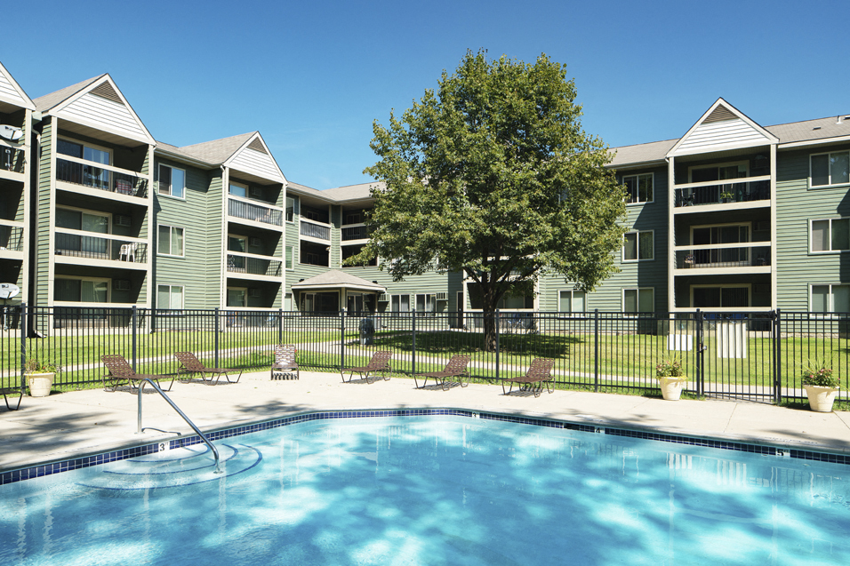 Outdoor pool with lounge chairs, surrounded by a black fence with the apartment building in the background