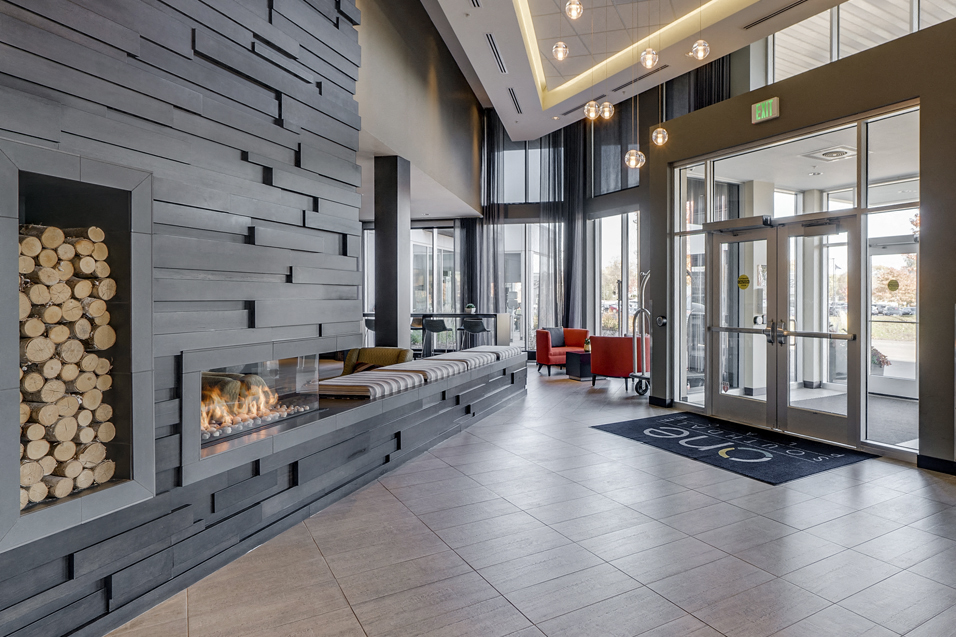 Lobby with a pile of logs next to a fireplace and red chairs in the background