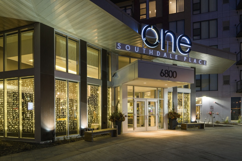 Outside shot of apartment building entrance with large illuminated sign reading "One Southdale Place" and the number "6800" above the front doors