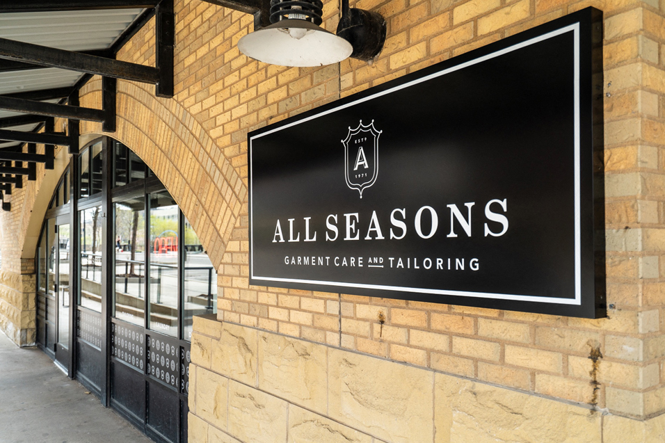 black sign with white text in a regal design that reads "All Seasons Garment Care and Tailoring"
