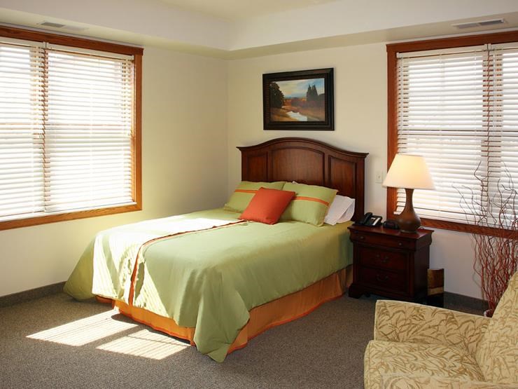 a bedroom with a bed and a chair and two windows