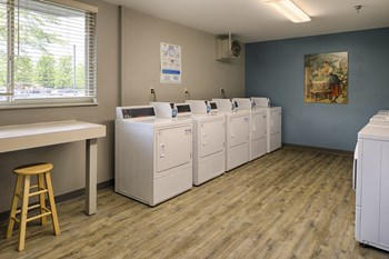 Laundry room with many washing machines and dryers and a folding table - Photo Gallery 14