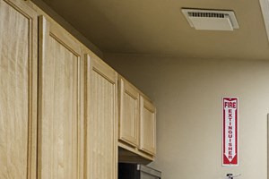 Community kitchen with light wooden cupboards and a galley layout. A stove, oven, and microwave on the left, a refrigerator on the right