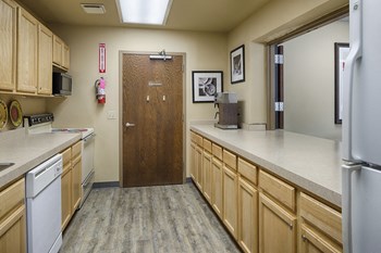 Community kitchen with light wooden cupboards and a galley layout. A stove, oven, and microwave on the left, a refrigerator on the right - Photo Gallery 8