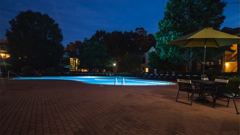 a swimming pool at night with chairs and umbrellas around it