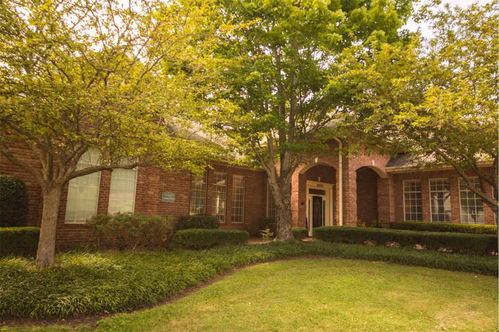 the front of a brick house with a lawn and trees