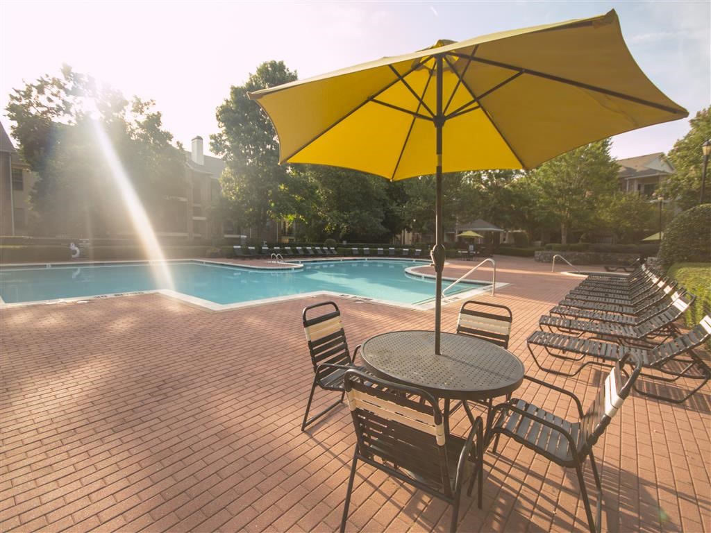 a patio with chairs and an umbrella next to a swimming pool