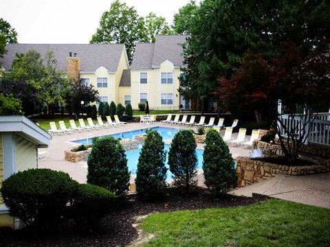 a swimming pool with chairs and trees in front of a house