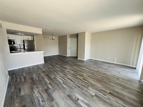 A room with wooden flooring and a kitchen area to the left.