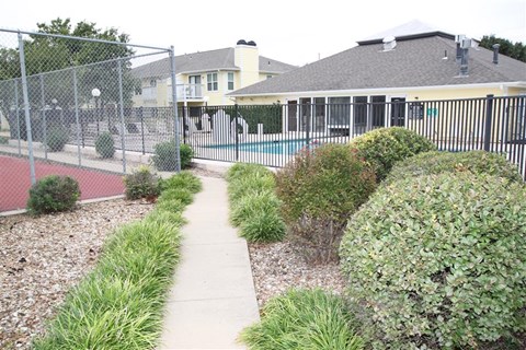 a sidewalk in front of a fenced in yard with a house