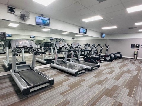 a gym with various cardio machines and televisions