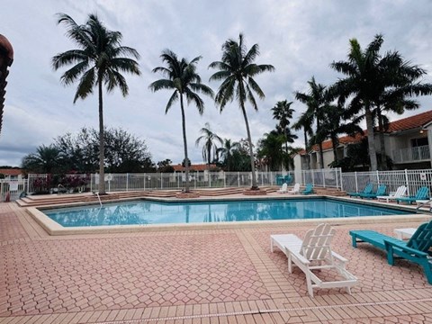 a large swimming pool with chairs and palm trees