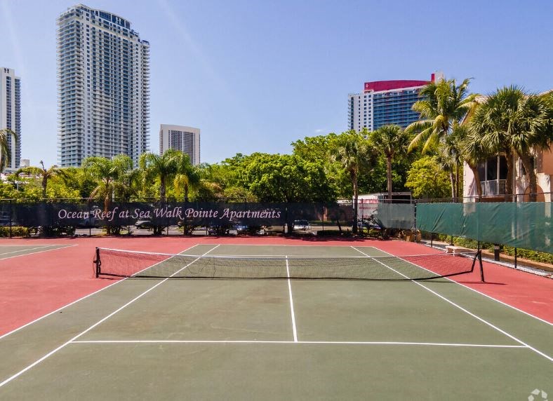 a tennis court with palm trees and buildings in the background