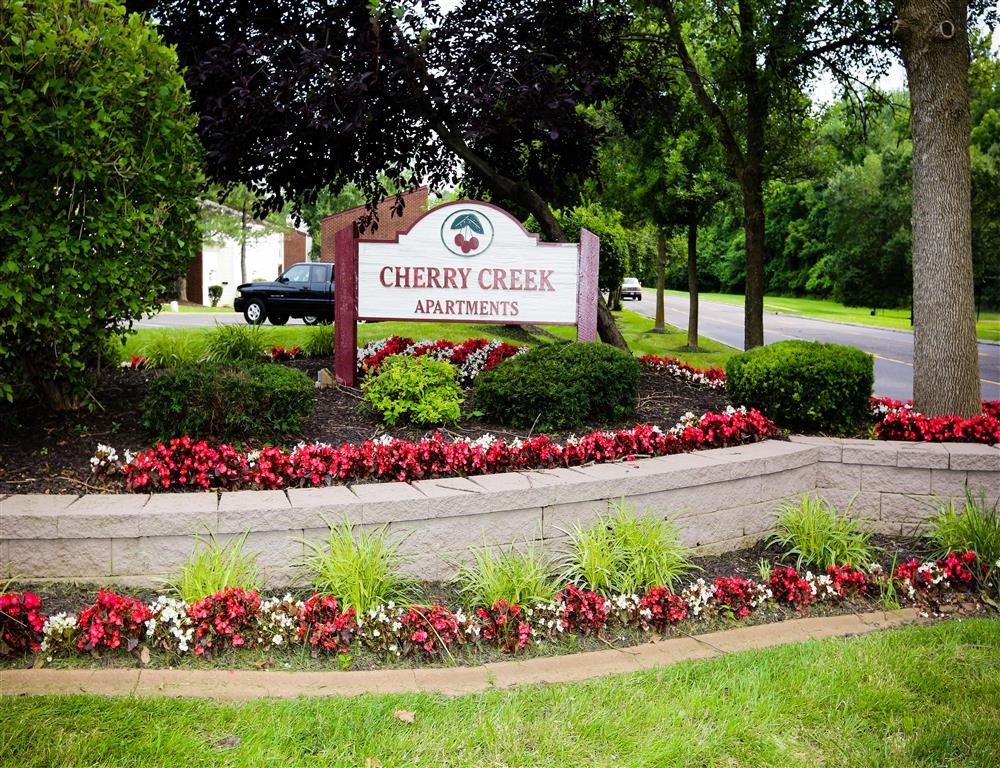 a flower garden in front of a cherry creek apartments sign