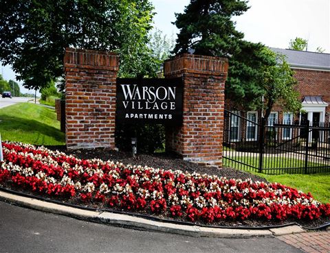 a sign for the watson village apartments in front of a brick fence and flowers