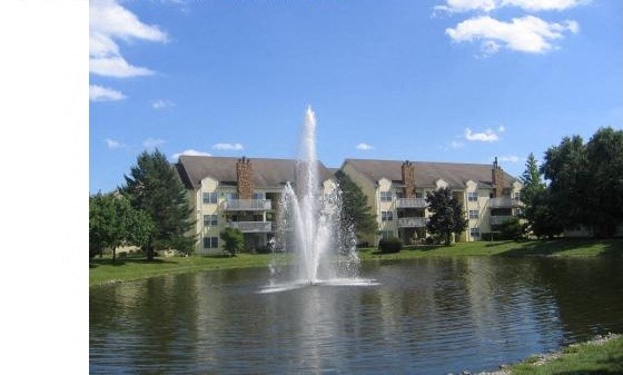 a fountain in the middle of a lake in front of an apartment building