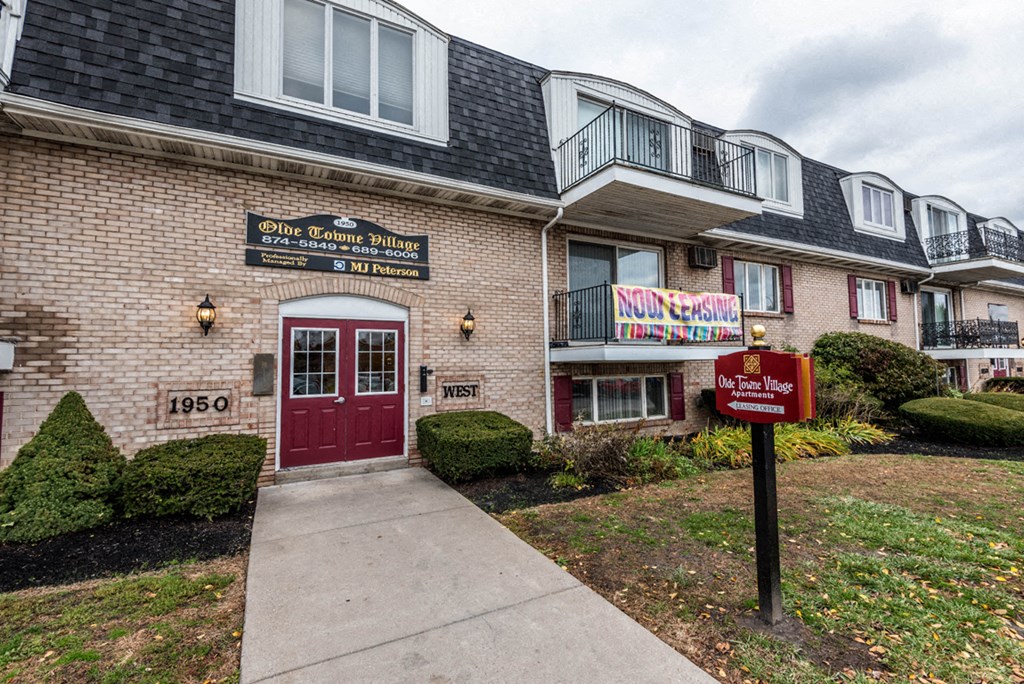 the front of a brick building with a red door and a sidewalk