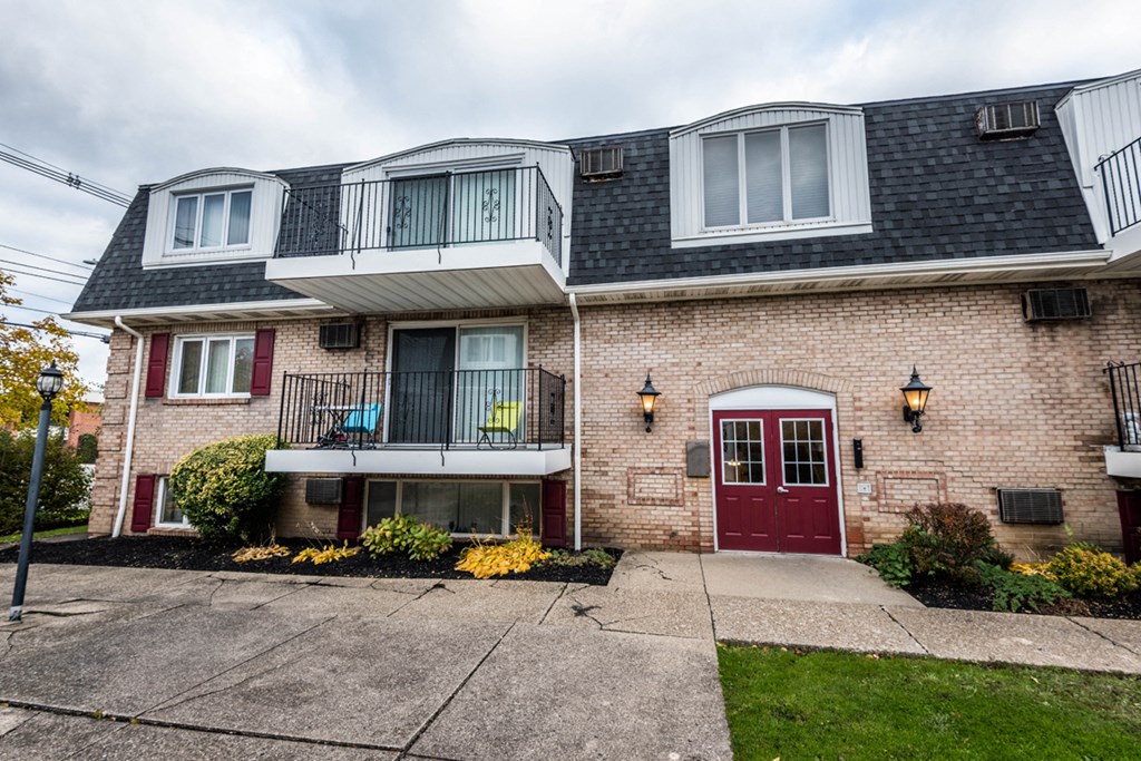 the front of a brick house with a red door and a balcony