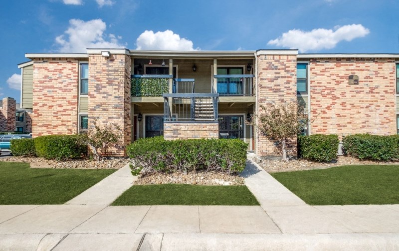 a brick apartment building with green grass and a sidewalk