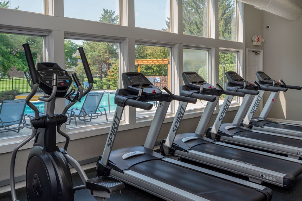 a gym with cardio equipment and windows overlooking a pool