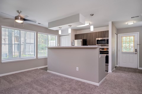 an empty living room with a kitchen and a ceiling fan