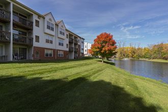 an apartment building overlooking the water with a tree in the grass