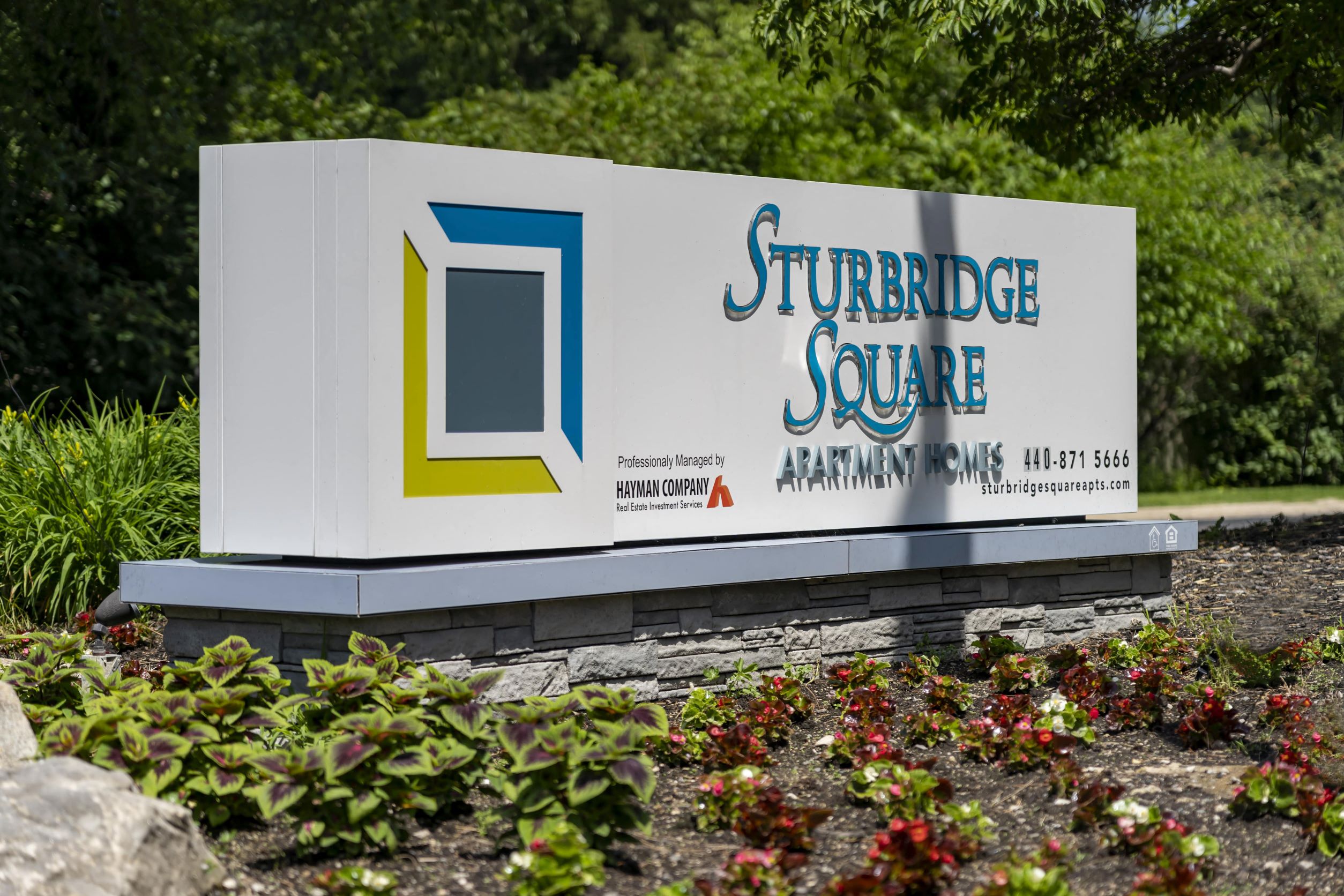 a sign for the sturbridge square park in front of a garden