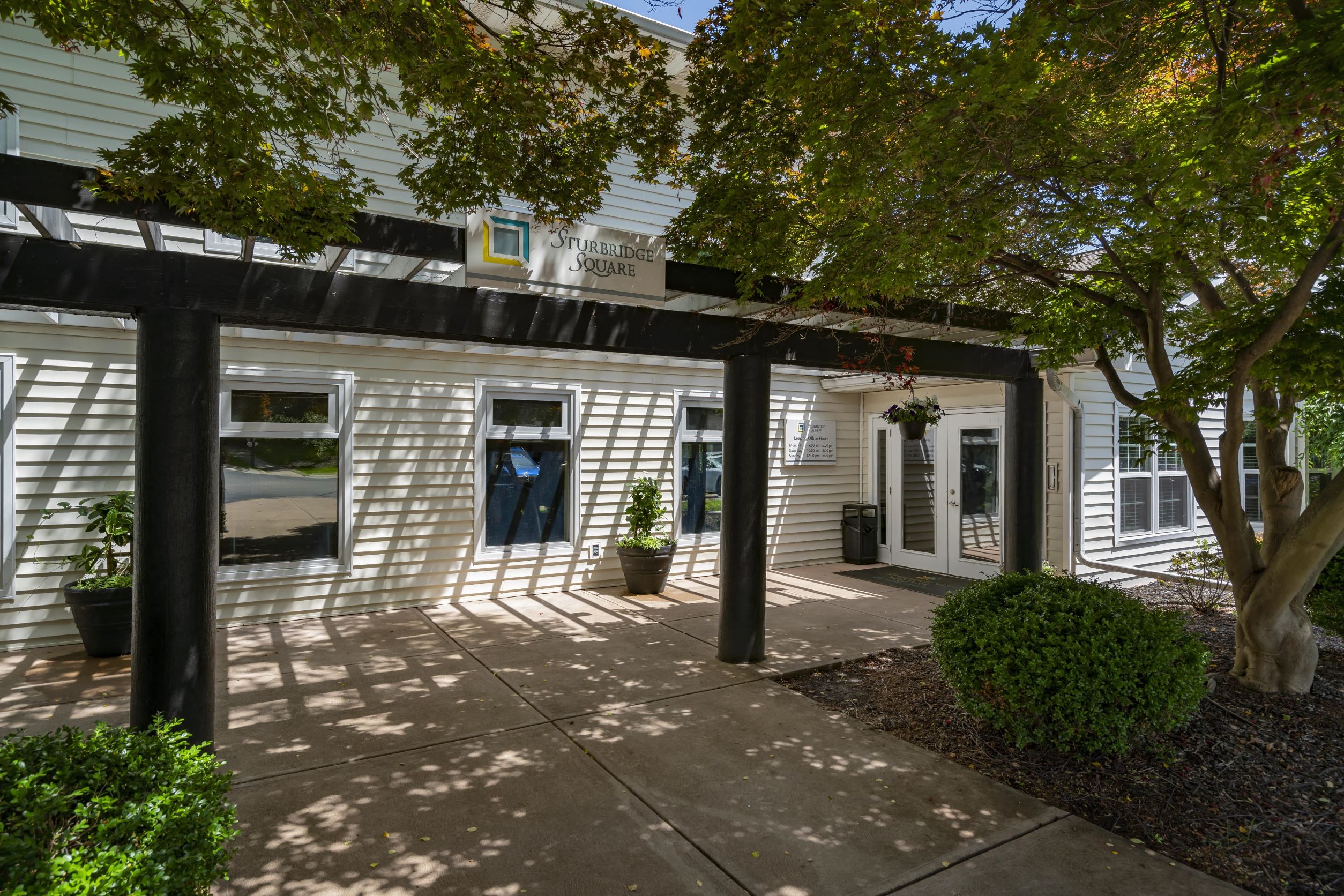 the front of a white building with a sidewalk and trees