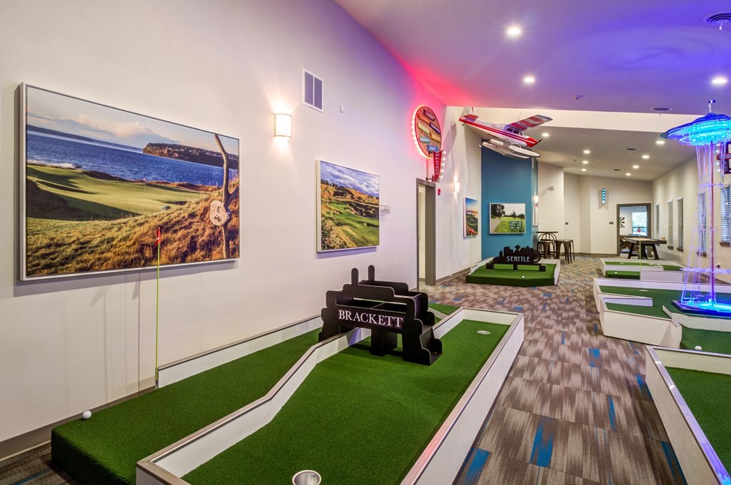 a game room with a golf simulator and paintings on the wall