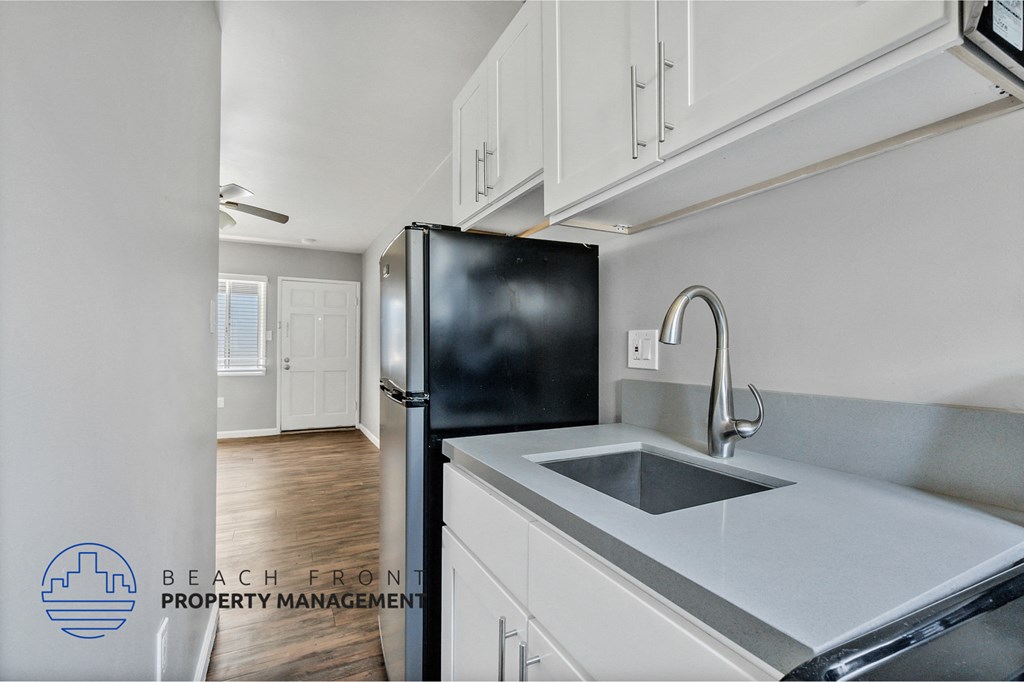 a kitchen with white cabinets and a sink and a black refrigerator